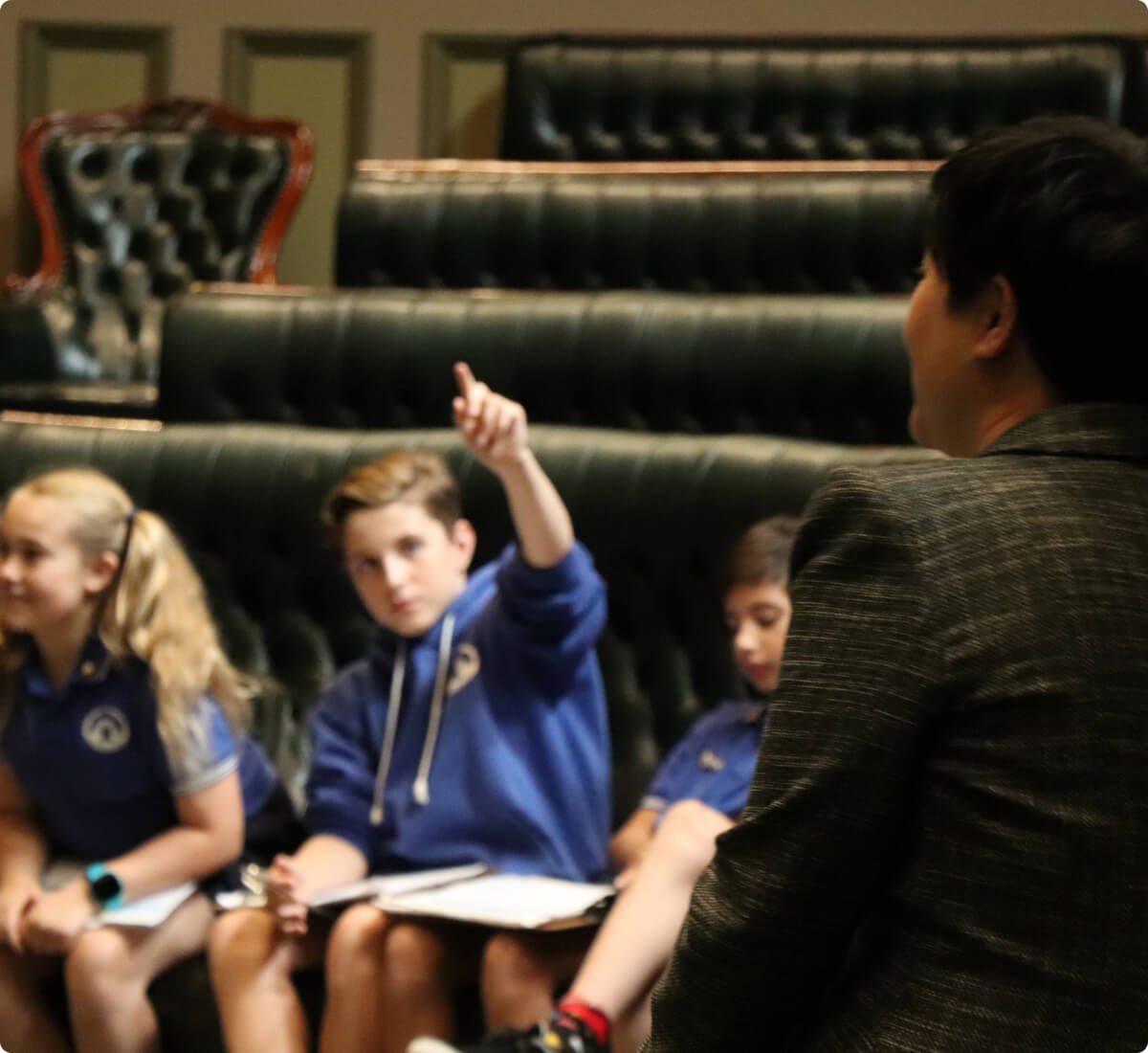 A teacher engages with three attentive students in a classroom. One student eagerly raises a hand to answer, creating an atmosphere of learning and interaction.